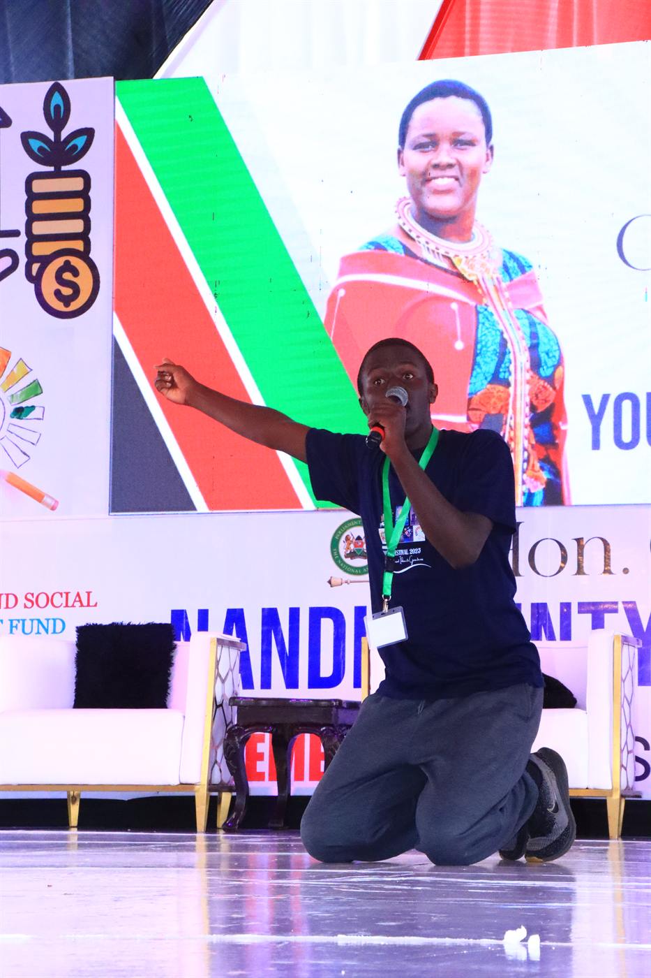 A performer kneeling on stage and speaking into a microphone at the 2025 festival